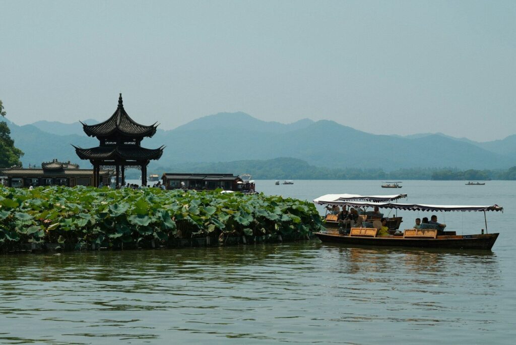 On West Lake in Hangzhou, A boat floating on top of a lake next to a tall building